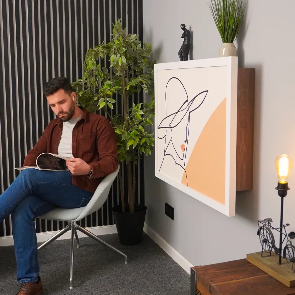 Man sat next to a fold away desk that has been folded up for space saving in the home.